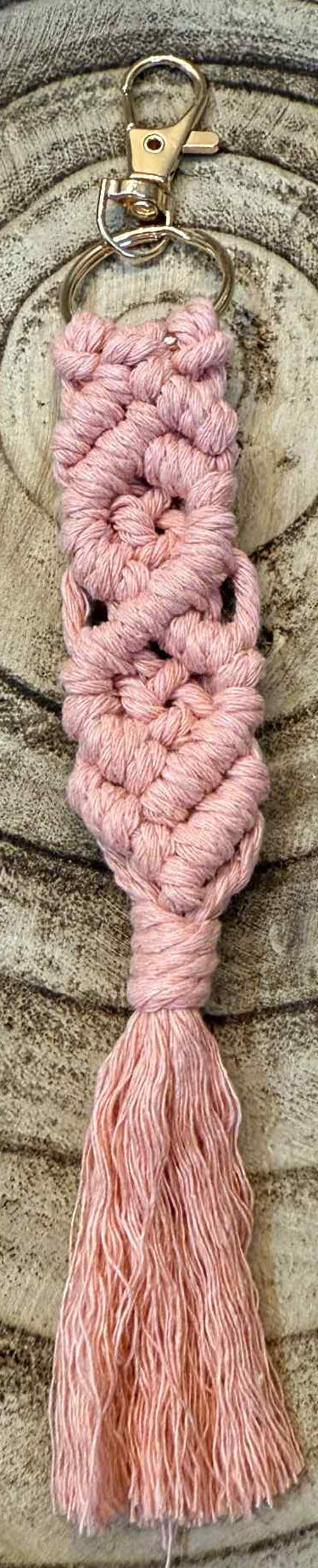 Pink macrame keychain with tassel on a wooden surface